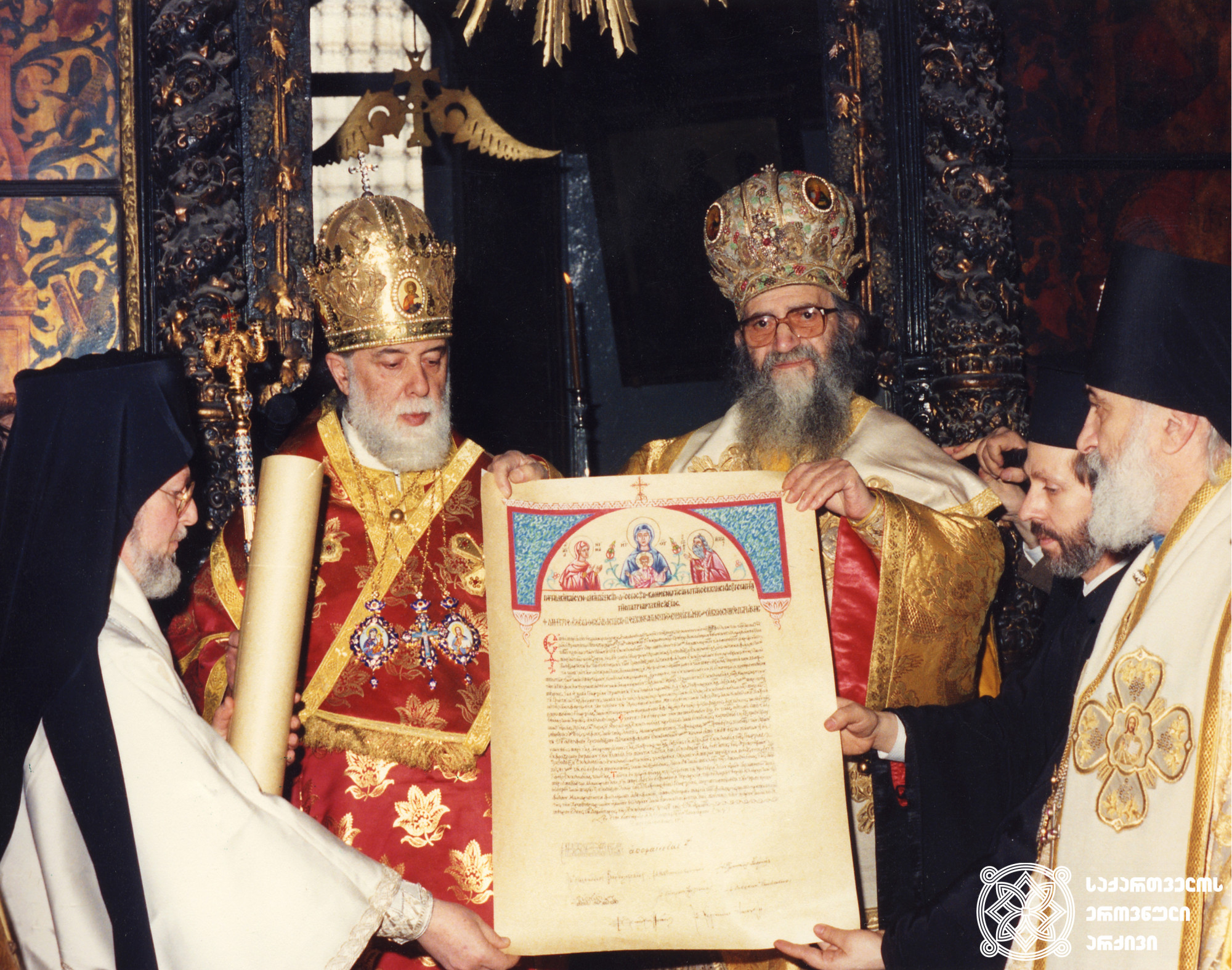 ილია II სრულიად საქართველოს კათოლიკოს-პატრიარქი და დიმიტრიოს I კონსტანტინეპოლის მთავარეპისკოპოსი და მსოფლიო პატრიარქი „საქართველოს უწმინდესი მართლმადიდებელი ეკლესიის ავტოკეფალიის ცნობისა და მტკიცების სიგელით“. ფოტოზე მარცხნივ ქალკედონიელი მიტროპოლიტი ბართლომეოსი (დღეს: მსოფლიო პატრიარქი) <br>
1990 წელი, 4 მარტი <br>
Ilia II, Catholicos-Patriarch of All Georgia, and Demetrios I, Archbishop of Constantinople and Ecumenical Patriarch, with the “Tomos of Recognition and Confirmation of the Autocephaly of the Most Holy Orthodox Church of Georgia.” On the Left: Metropolitan Bartholomew of Chalcedon (currently the Ecumenical Patriarch) <br>
March 4, 1990