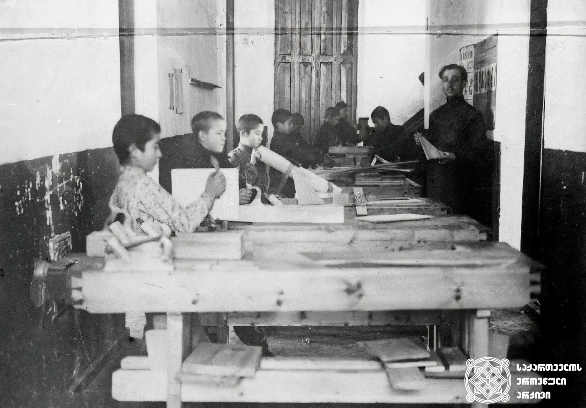 სოხუმის  ოლქის  სახალხო სასწავლებლის  ინსპექციის  აბრუბჟის ორკლასიანი  სკოლის  მოსწავლეები სადურგლო-სახელოსნო  ოთახში  <br>
(1910-1917) <br>
Pupils of the Sokhumi District Public School Inspectorate of the two-grade school Abrubzh in the carpentry-workshop room <br>
(1910-1917)