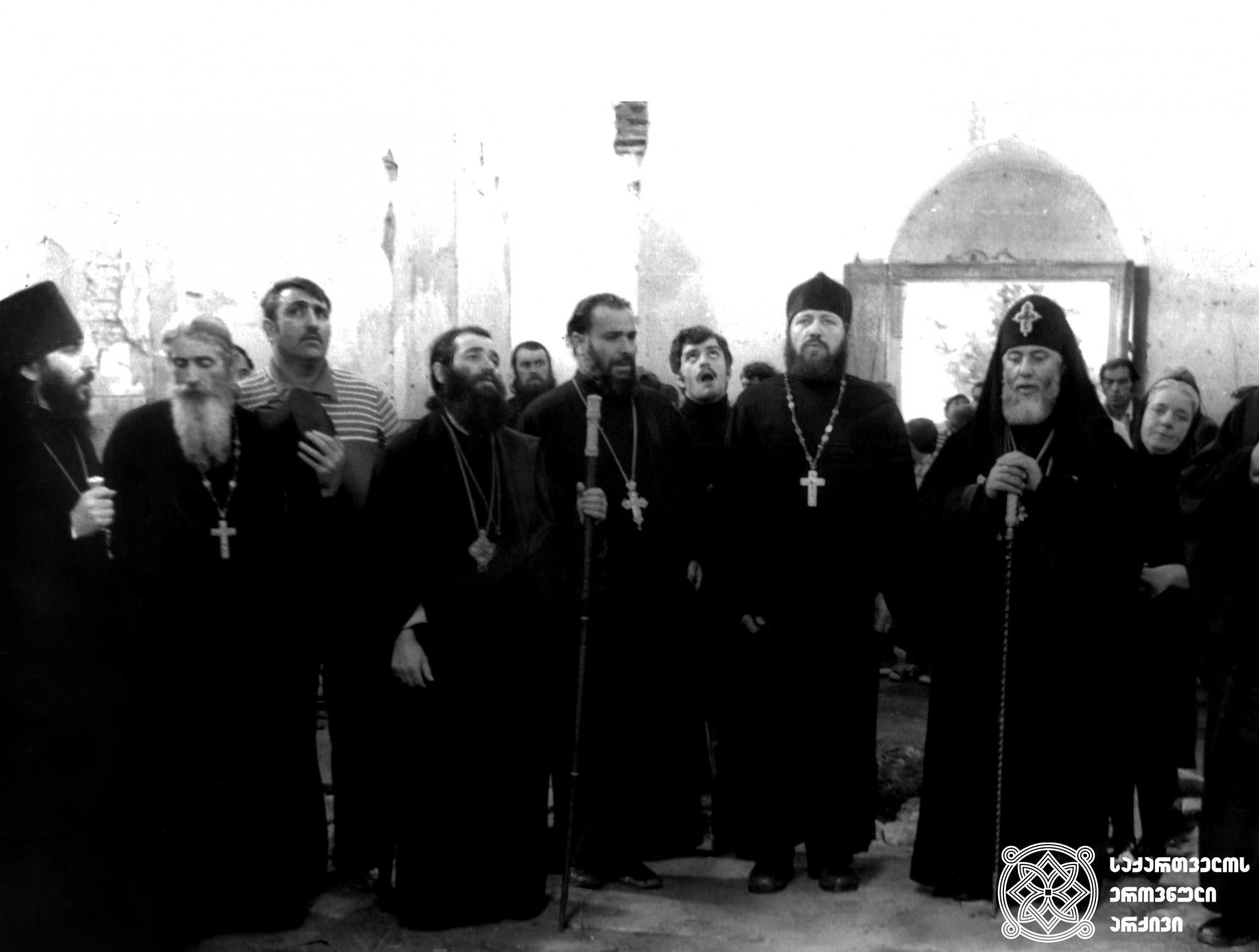 მარცხნიდან მარჯვნივ: ეპისკოპოსი იოანე (ანანიაშვილი), არქიმანდრიტი იოაკიმე (ასათიანი), ეპისკოპოსი თადეოზი (იორამაშვილი), დეკანოზი ათანასე (ჩახვაშვილი, მომავალი მღვდელმთავარი), მღვდელი ამბროსი (ქათამაძე, მომავალი მღვდელმთავარი), ილია II სრულიად საქართველოს კათოლიკოს-პატრიარქი. 
უკან: რევაზ სიხარულიძე (დღეს მამა ელისე (სიხარულიძე)), მორჩილი ზოია შუშანია. <br>
სენაკი, მენჯის მონასტერი, 1978 წელი <br>
Left to right: Bishop Ioane (Ananiashvili), Archimandrite Ioakime (Asatiani), Bishop Thaddeus (Ioramashvili), Priest Athanase (Chakvashvili, future hierarch), Priest Ambrosi (Katamadze, future hierarch), Ilia II - Catholicos-Patriarch of All Georgia.  <br>
Back: Revaz Sikharulidze (currently Father Elise), novice Zoia Shushania. <br> 
Senaki, Menji Monastery, 1978.