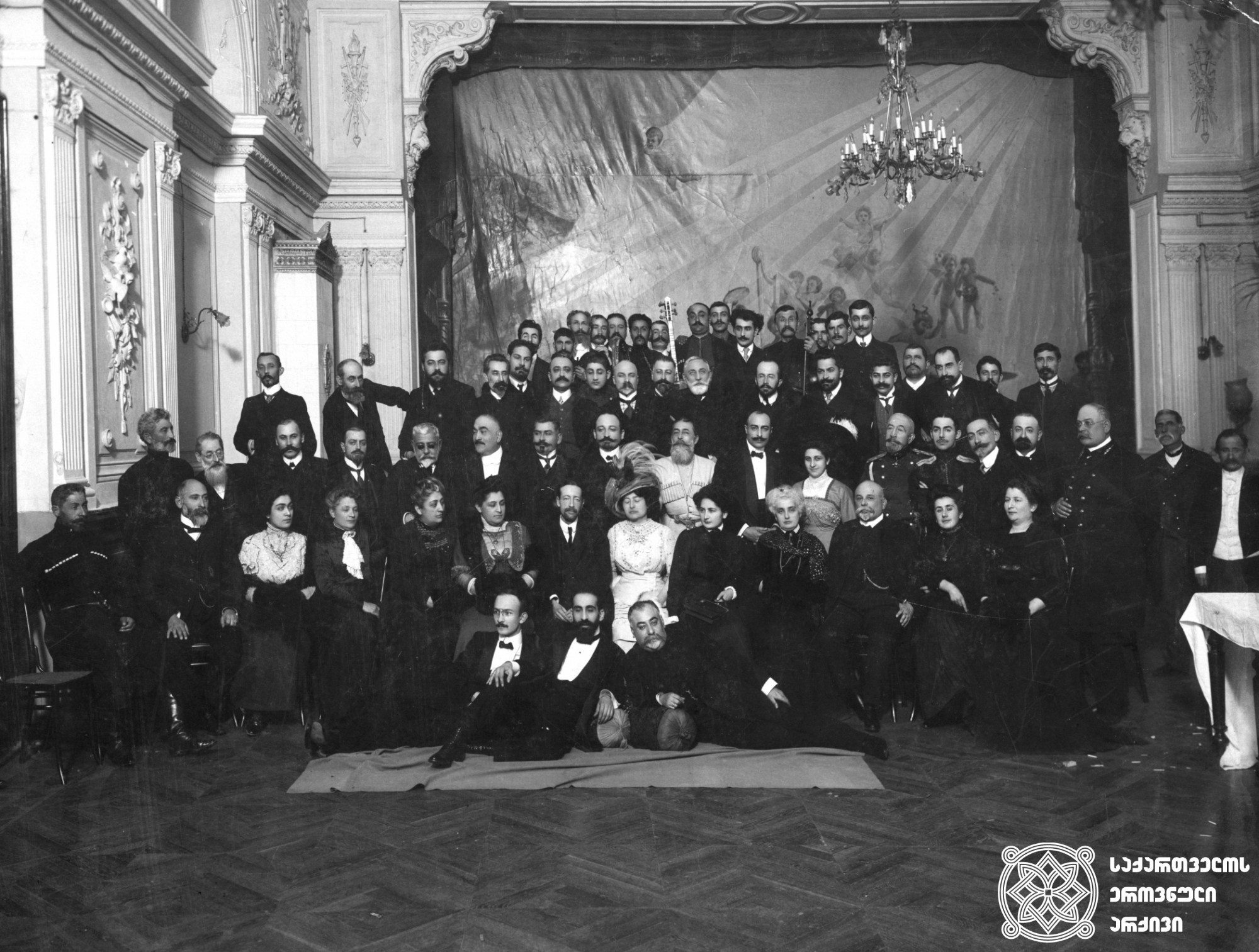 ქართველ თავადაზნაურთა შეხვედრა ინგლისელ დიპლომატ ოლივერ უორდროპთან. ზემოდან მესამე რიგში, შუაში ზის ალექსანდრე სარაჯიშვილი -  მთარგმნელი, ჟურნალისტი, საზოგადო მოღვაწე; 1899 წელს არჩეული იყო სოხუმის ქალაქის თავად. <br>
1911 წელი <br>
Meeting of the Georgian nobility with the English diplomat Oliver Wardrop In the third row from the top, in the middle sits Aleksandre Sarajishvili, translator, journalist,
 and public figure. In 1899, he was elected the head of the city of Sokhumi. <br>
1911
