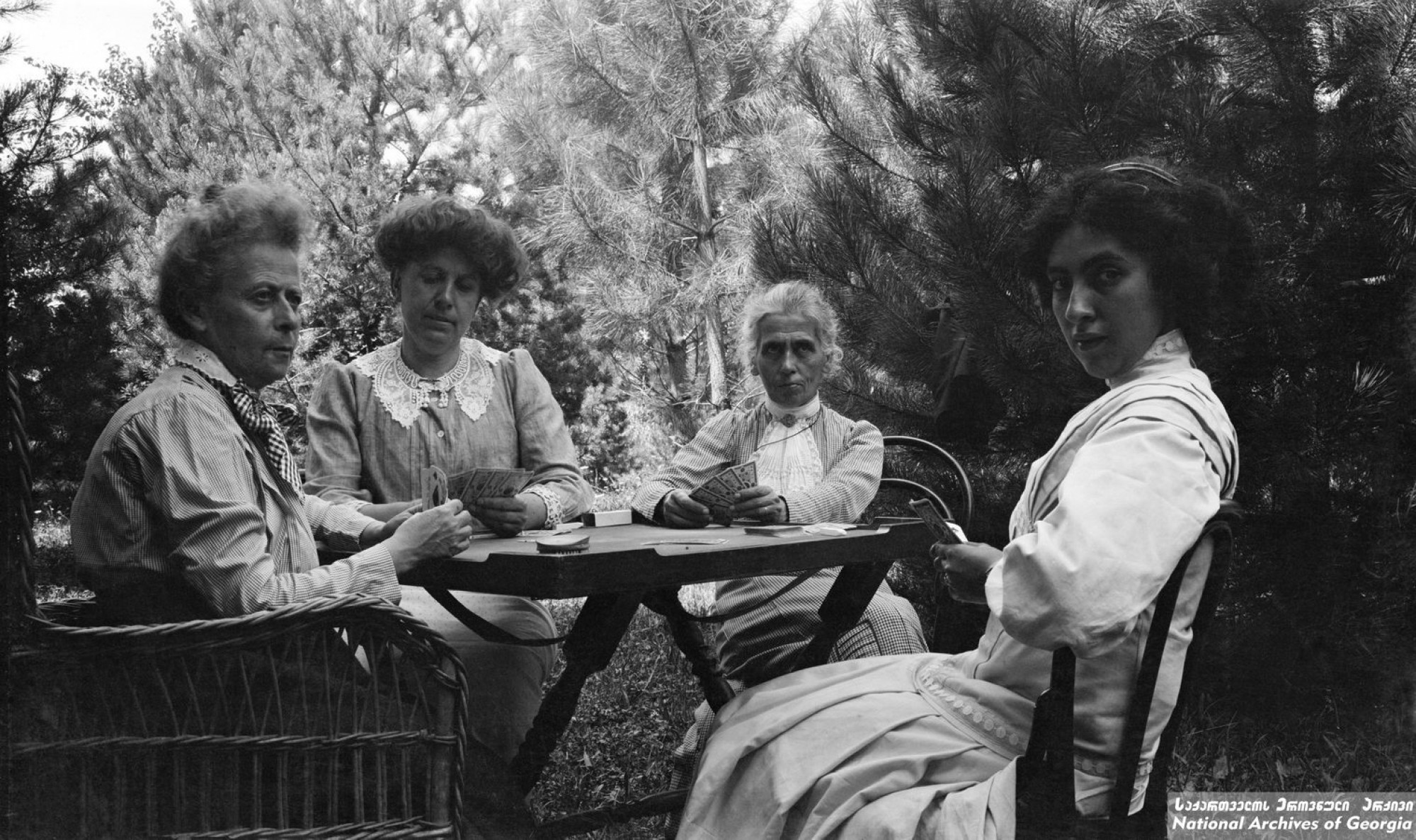 ნიკო ნიკოლაძის დები ანასტასია და ეკატერინე ნიკოლაძეები თამაშობენ ბანქოს კლარა ტიტელი-გურამიშვილთან და რუსუდან ნიკოლაძესთან ერთად.<br>
დიდი ჯიხაიში, სამტრედია. <br> ფოტო: გიორგი ნიკოლაძე. <br>
1910. <br> 
Niko Nikoladze’s sisters, Anastasia and Ekaterine playing cards together with Rusudan Nikoladze and Klara Titeli-Guramishvili. <br> 
Didi Jikhaishi, Samtredia, Georgia. <br> 
Photo: Giorgi Nikoladze. <br> 
ეკატერინე და ანასტასია ნიკოლაძეები ერთ-ერთი პირველი ქართველი ქალები იყვნენ, რომლებმაც განათლება ევროპის უნივერსიტეტში მიიღეს.